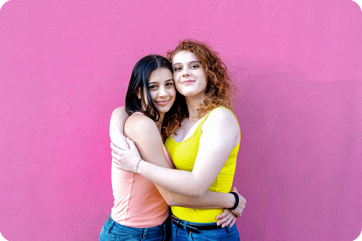 Female Couple embrace in front of pink backdrop wall