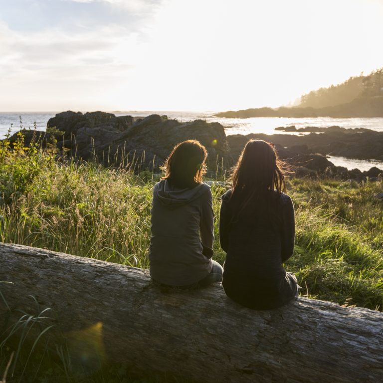 Two Women sit on a Log, Look Out Across Bay
