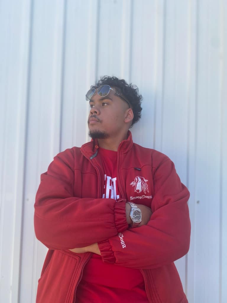 A boy in a red bomber jacket leans up against a wall