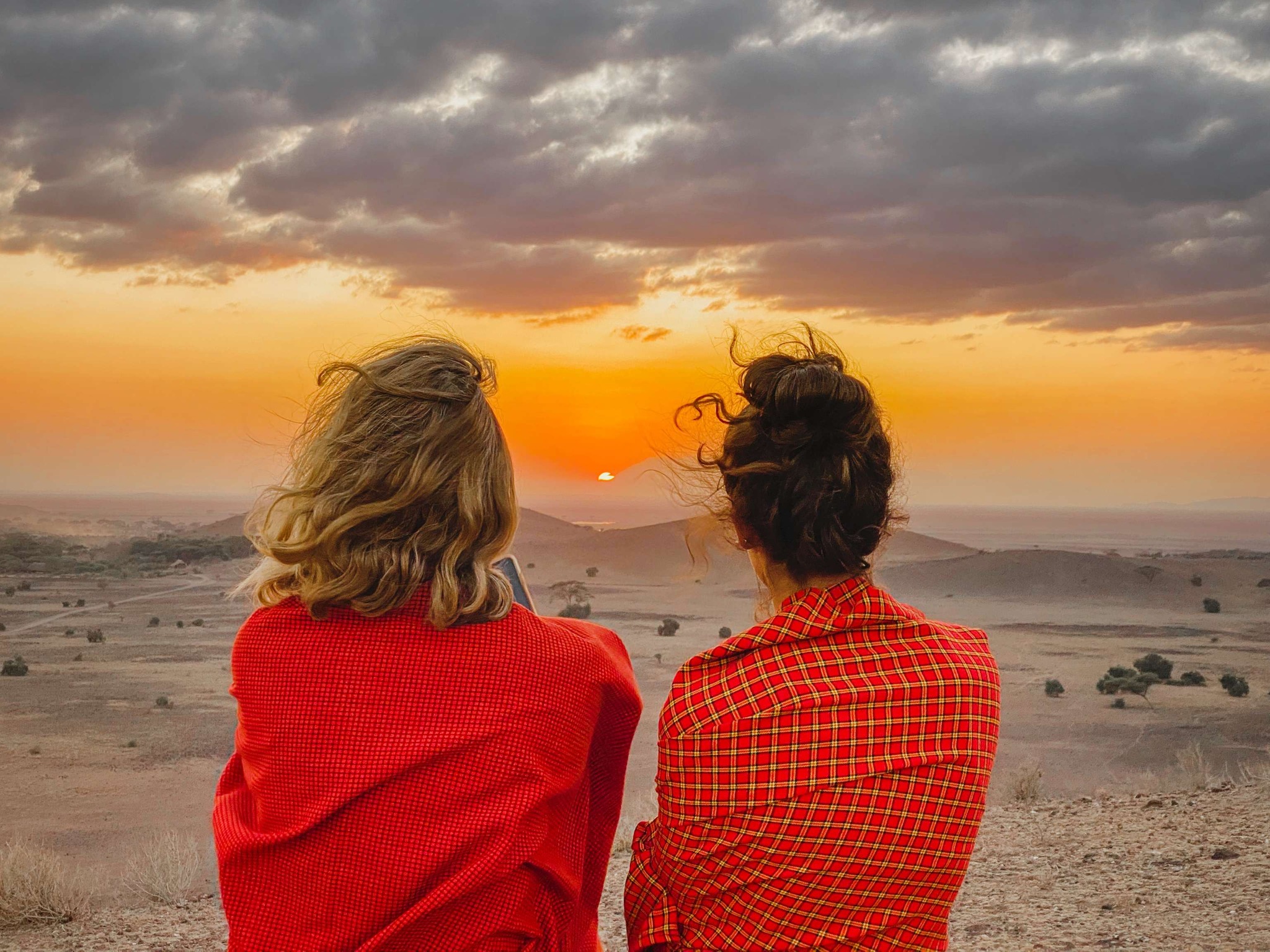 Two women facing sunset wrapped in orange blankets