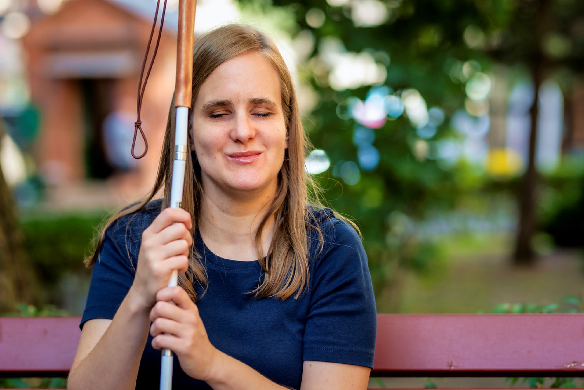 A visually impaired woman holding a white cane and sitting on the bench in the park