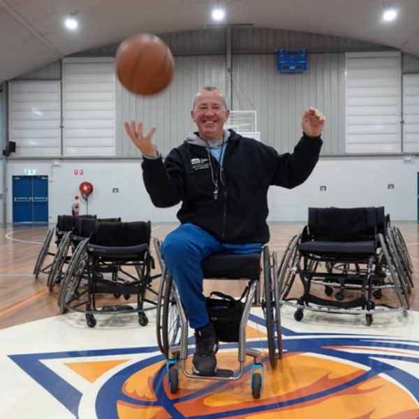 Man in a wheelchair on a basketball court bouncing a ball