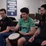 student playing the drums with peer mentors Jay and Jake