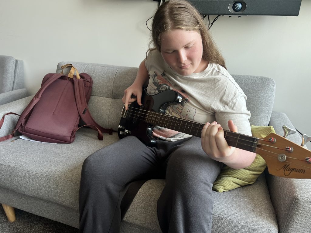 Leon plays bass guitar sitting on a couch