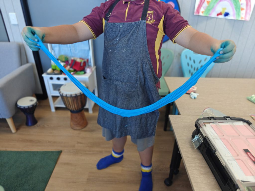A boy in school uniform wearing an apron stretches out blue slime in his hands