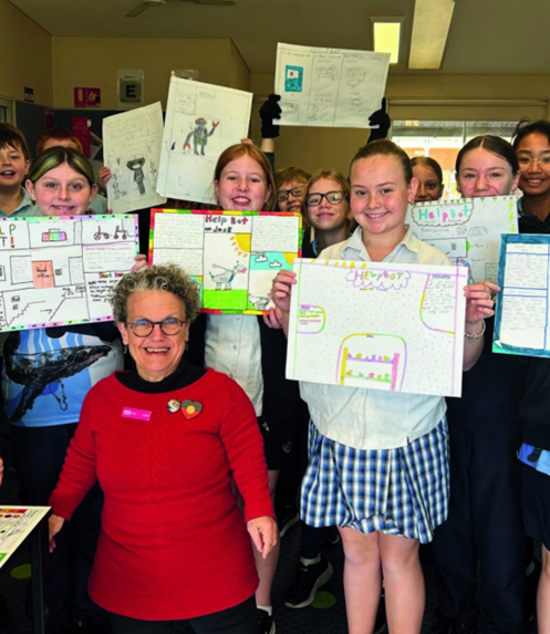 Maree and a group of primary school kids hold up their drawings