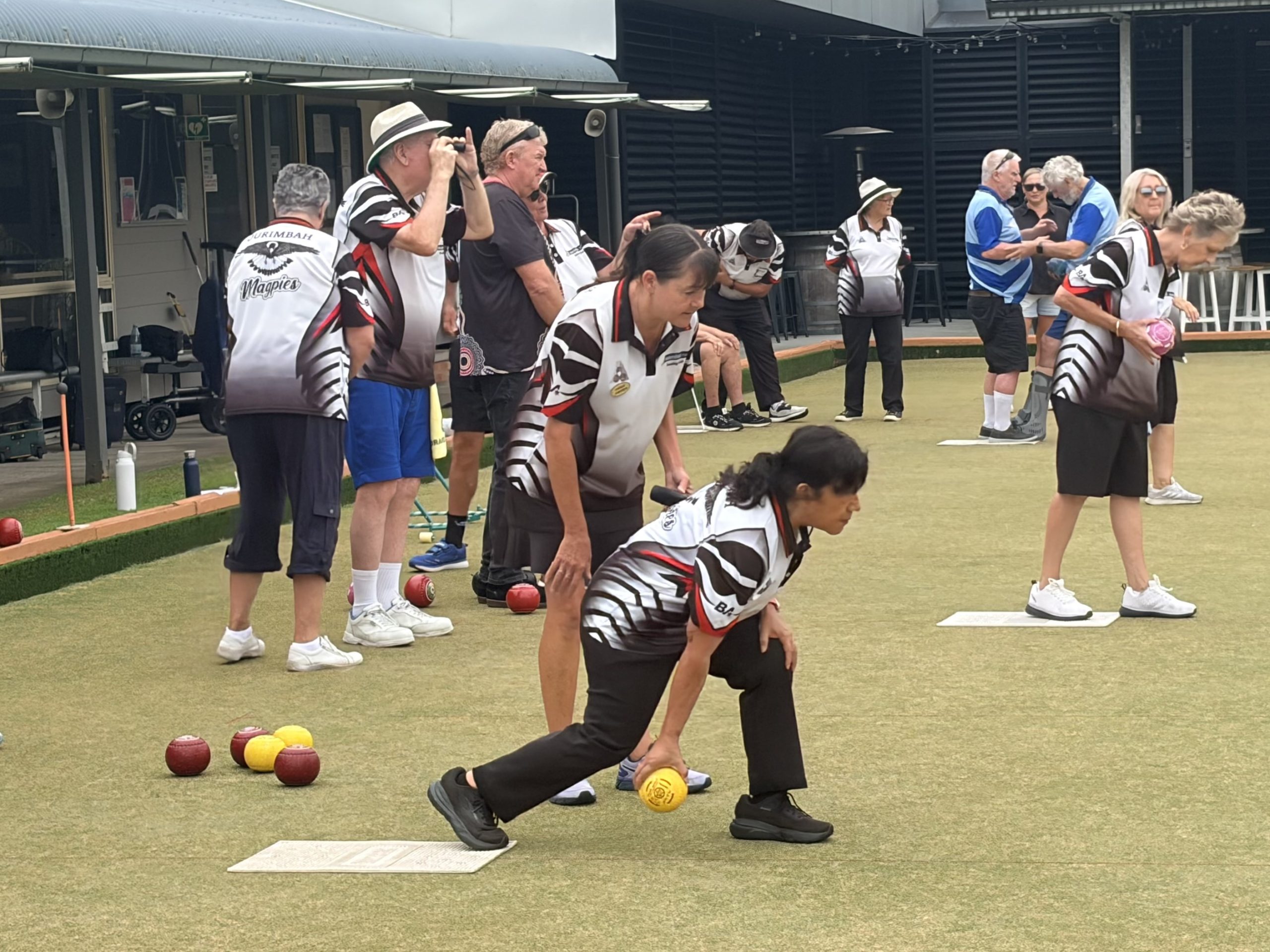 Violeta kneels to bowl a yellow ball on the lawn bowls field